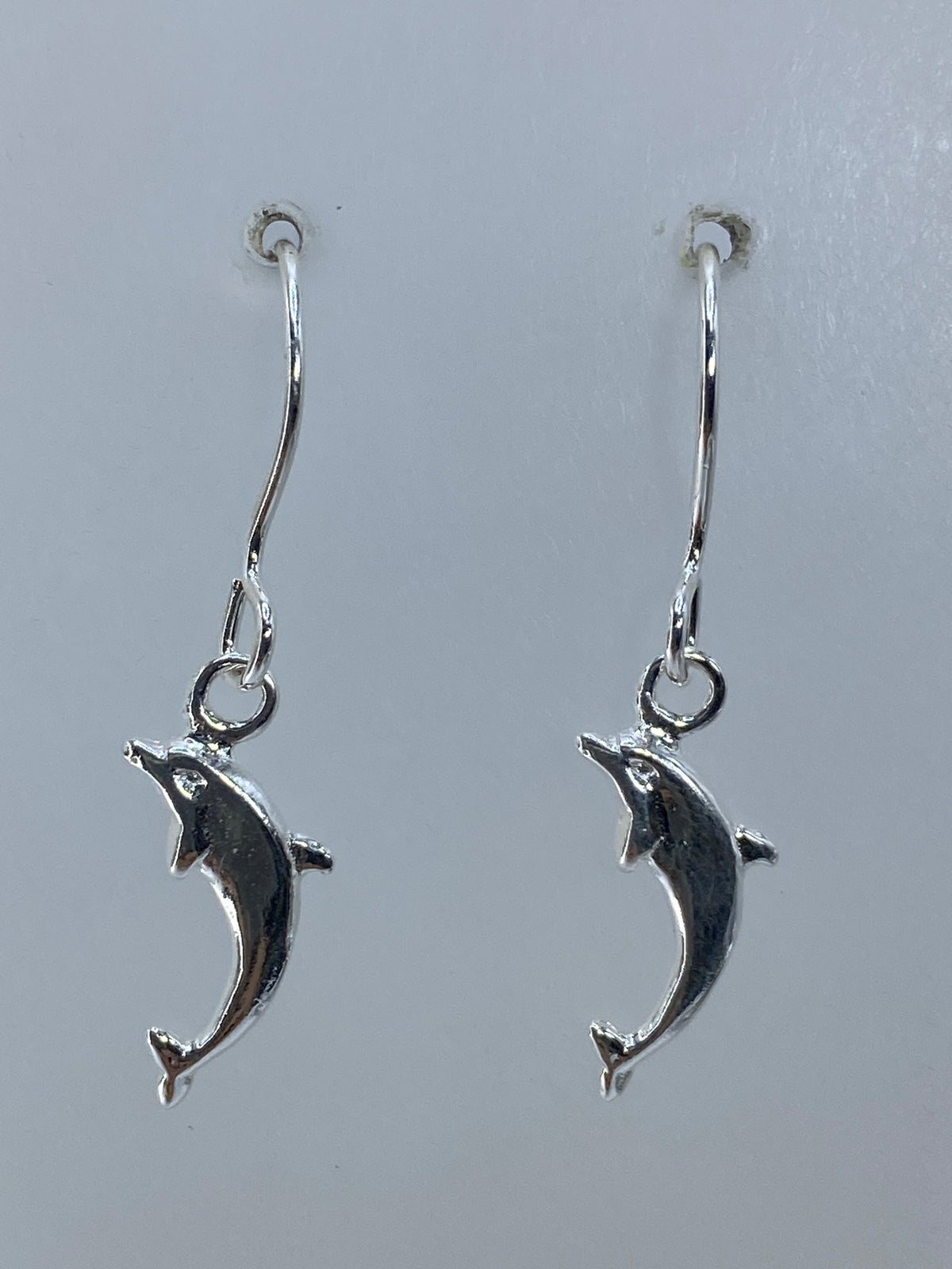 Par de aretes de plata con delfines en cartoneado, sobre fondo blanco
