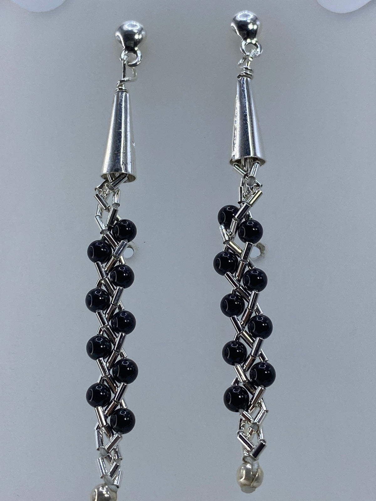 Par de aretes de plata con piedra negra engastada, colgando sobre fondo gris