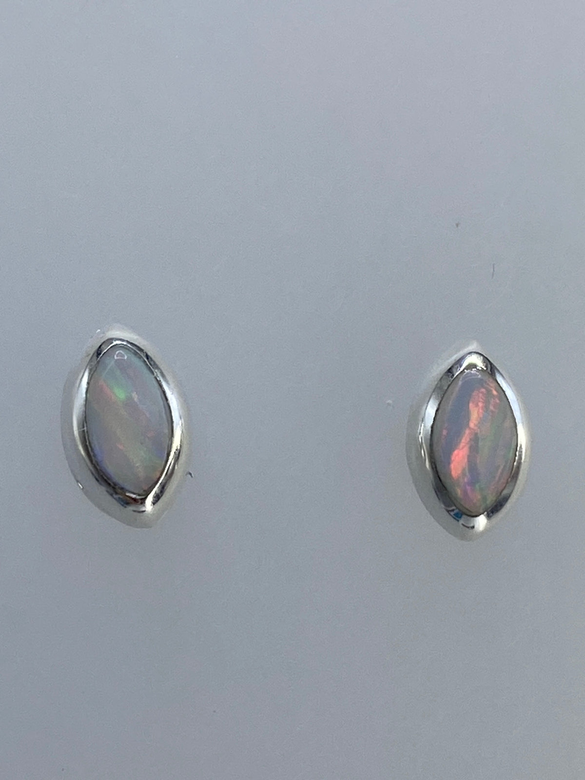 Par de aretes de plata con ópalo de fuego multicolor, mostrando destellos verdes y rojos