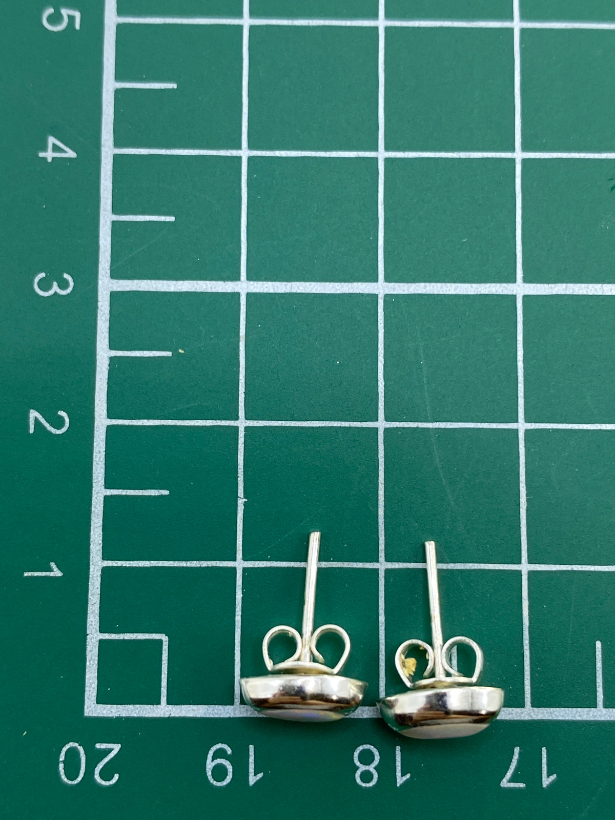 Aretes en la mano mostrando el tamaño minimalista y el juego de colores del ópalo