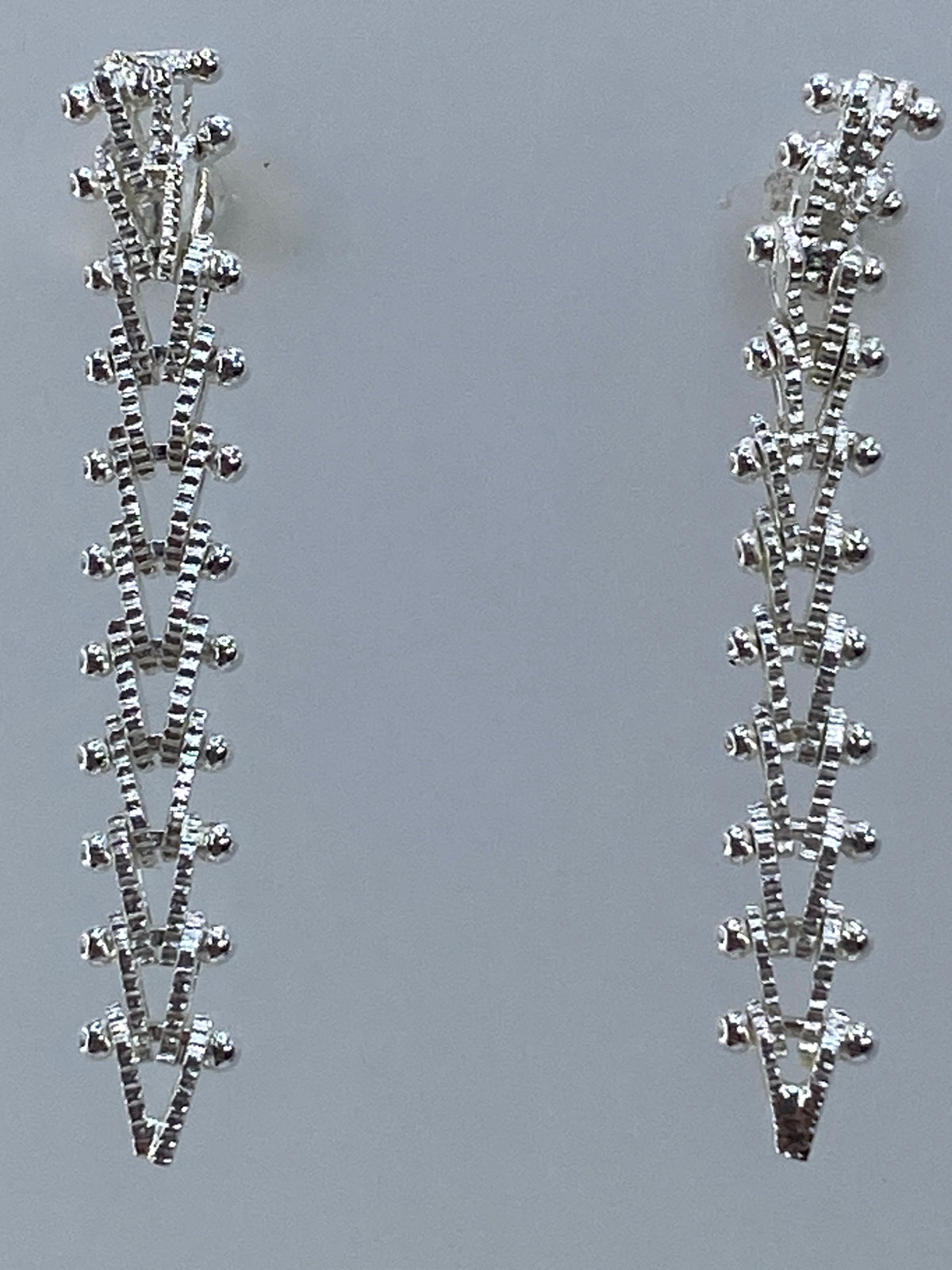 Detalle frontal de los aretes mostrando el patrón de triángulos invertidos en plata pulida