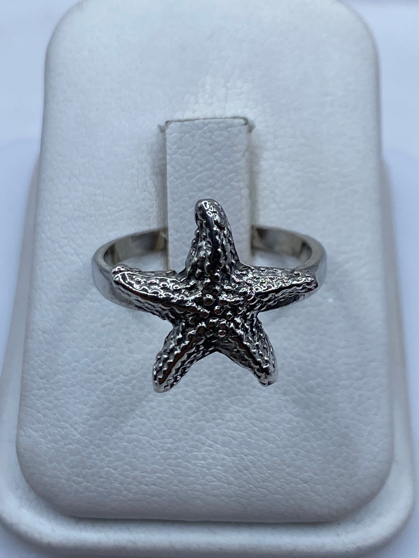 Anillo de plata .925 con estrella de mar en relieve, visto de frente en estuche blanco