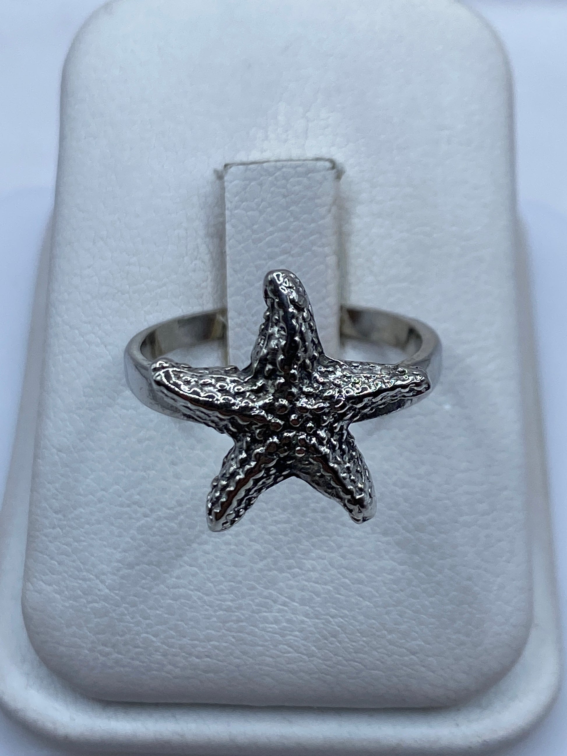 Anillo de plata .925 con estrella de mar en relieve, visto de frente en estuche blanco