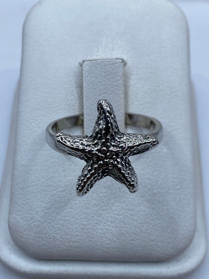 Anillo de plata .925 con estrella de mar en relieve, visto de frente en estuche blanco