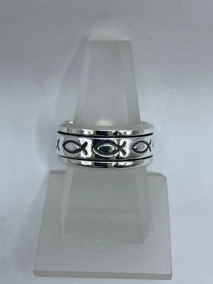 Vista frontal de anillo spinner plata .925 con pez ictus cristiano en banda giratoria sobre fondo oxidado — artesanal Taxco
