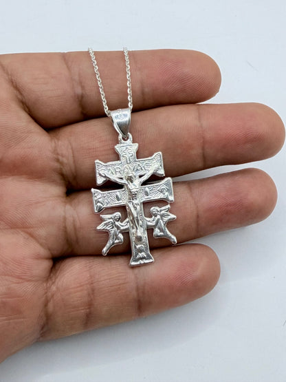 Collar con cruz Caravaca sostenido en mano, mostrando proporción de cadena fina y dije religioso
