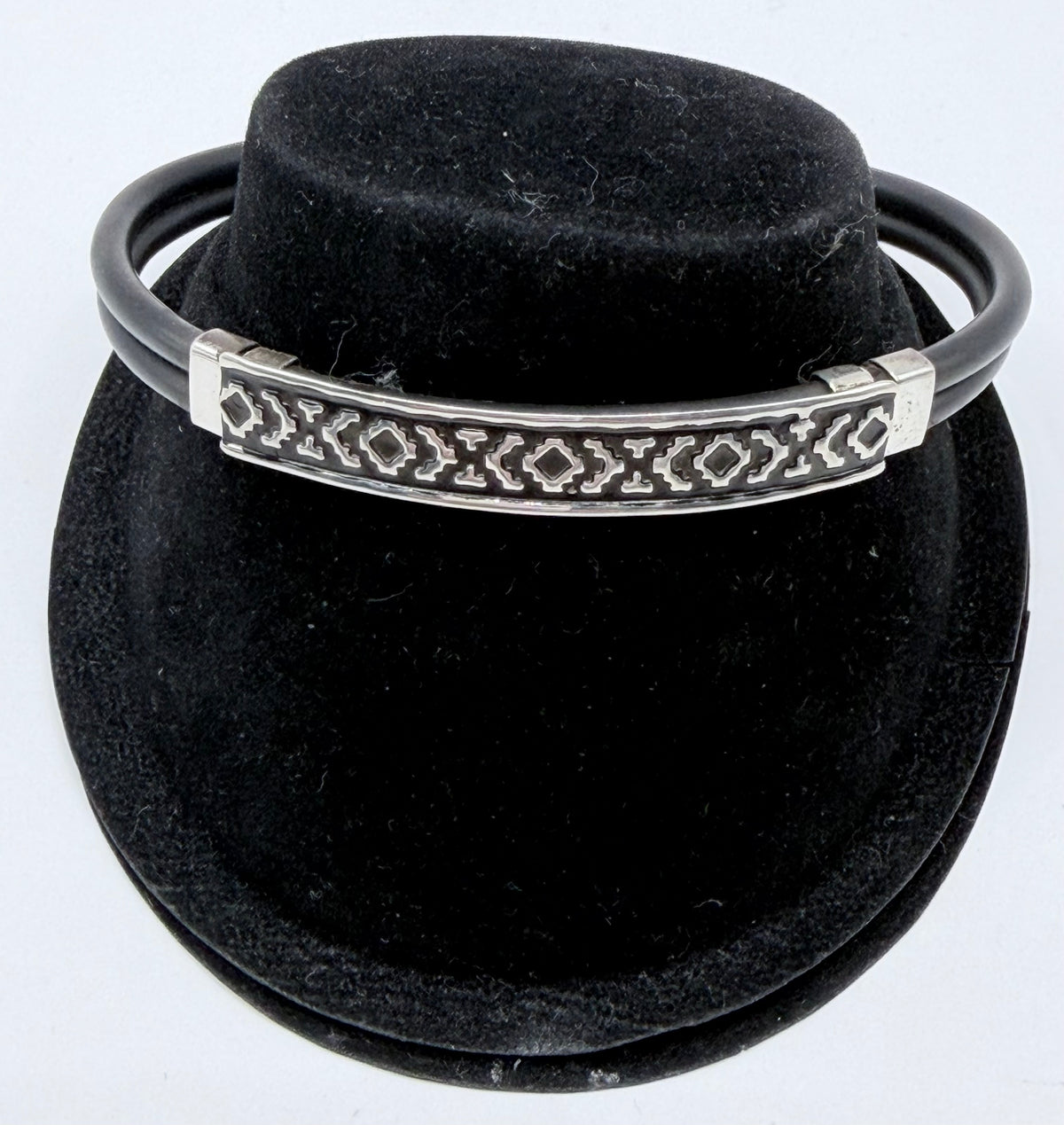 Pulsera rígida de plata .925 con caucho negro y grecas geométricas talladas, vista frontal sobre fondo negro