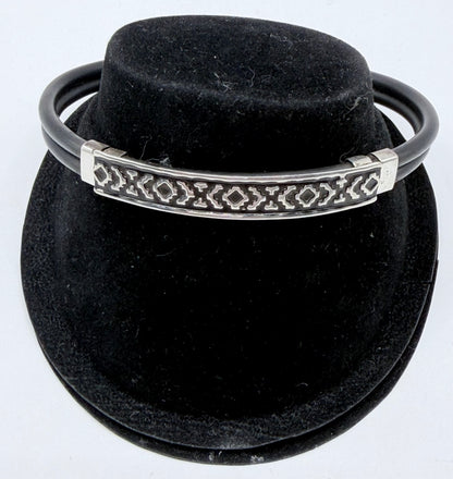 Pulsera rígida de plata .925 con caucho negro y grecas geométricas talladas, vista frontal sobre fondo negro