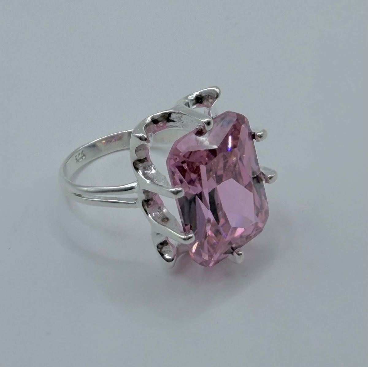Vista frontal del anillo con circonia rosa brillante refractando luz, sobre fondo gris claro